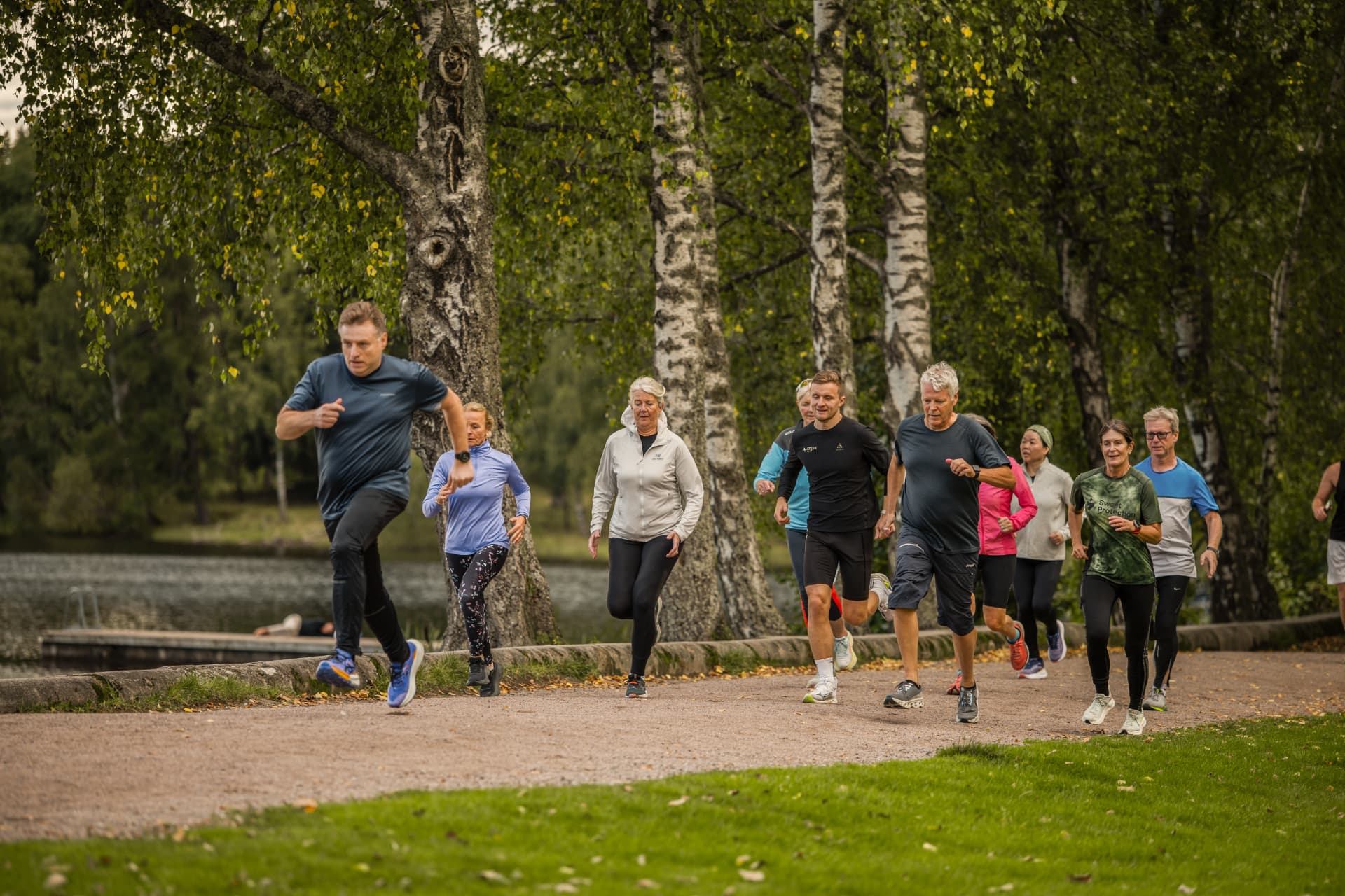 Gruppen løper sammen på grusvei ved vannet mellom bjørketrærne